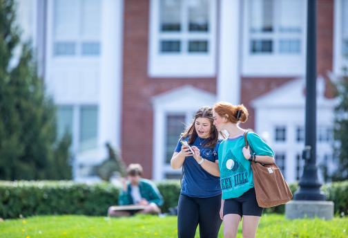 One student is showing her cell phone to another student while walking to class. 
