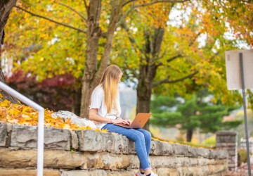 A student sitting on a wall using a laptop