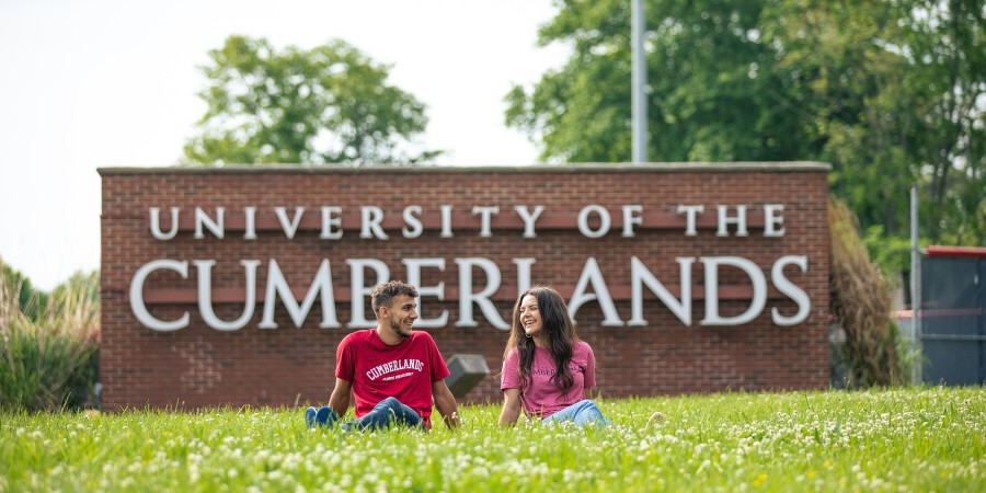 Two students relax in front of Cumberlands welcome sign 
