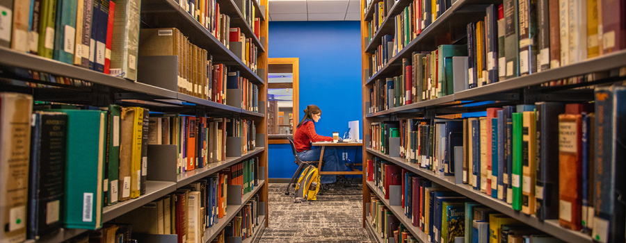 A student studying in the new library with books in the foreground. 