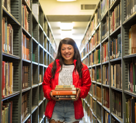 girl standing holding books in library